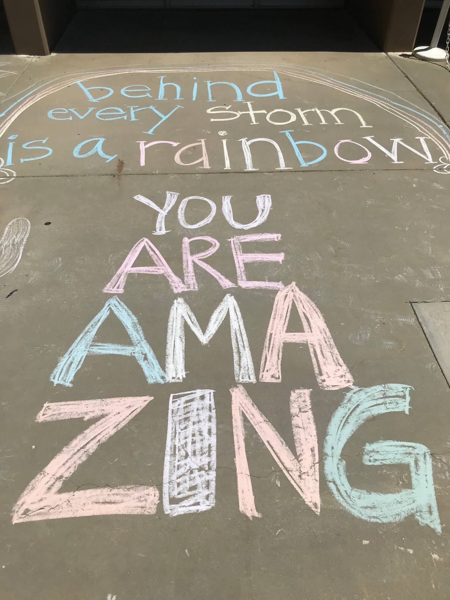Chalk drawing that says "behind every storm is a rainbow you are amazing"